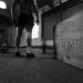 Personne devant une barre de musculation dans une salle de sport, photo en noir et blanc.