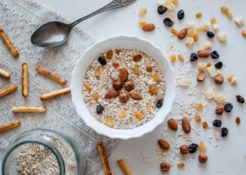 Table blanche sur lauqelle est déposé un bolle rempli de flocons d'avoine avec quelques noisettes