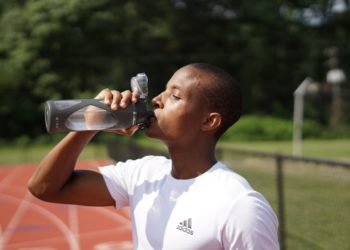 Personne qui boit une gourde d'eau sur une piste d'athlétisme
