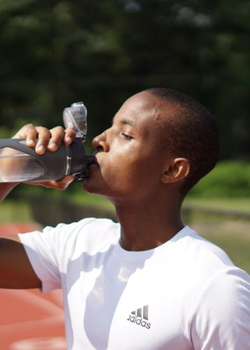 Personne qui boit une gourde d'eau sur une piste d'athlétisme