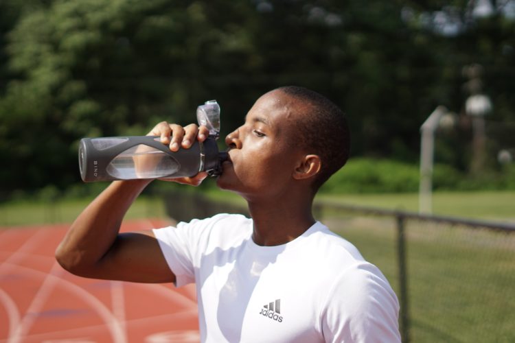 Personne qui boit une gourde d'eau sur une piste d'athlétisme