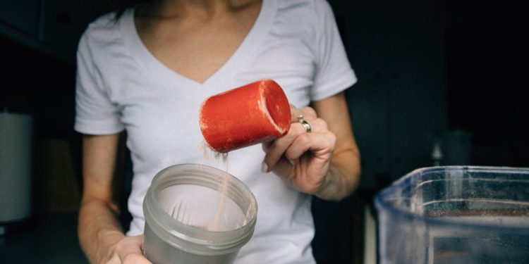 Femme qui remplit un shaker d'une poudre, probablement de la BCAA