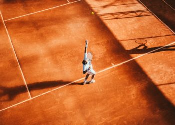 Court de tennis sur terre battue, un joueur est en train de faire un service, la balle est en l'air